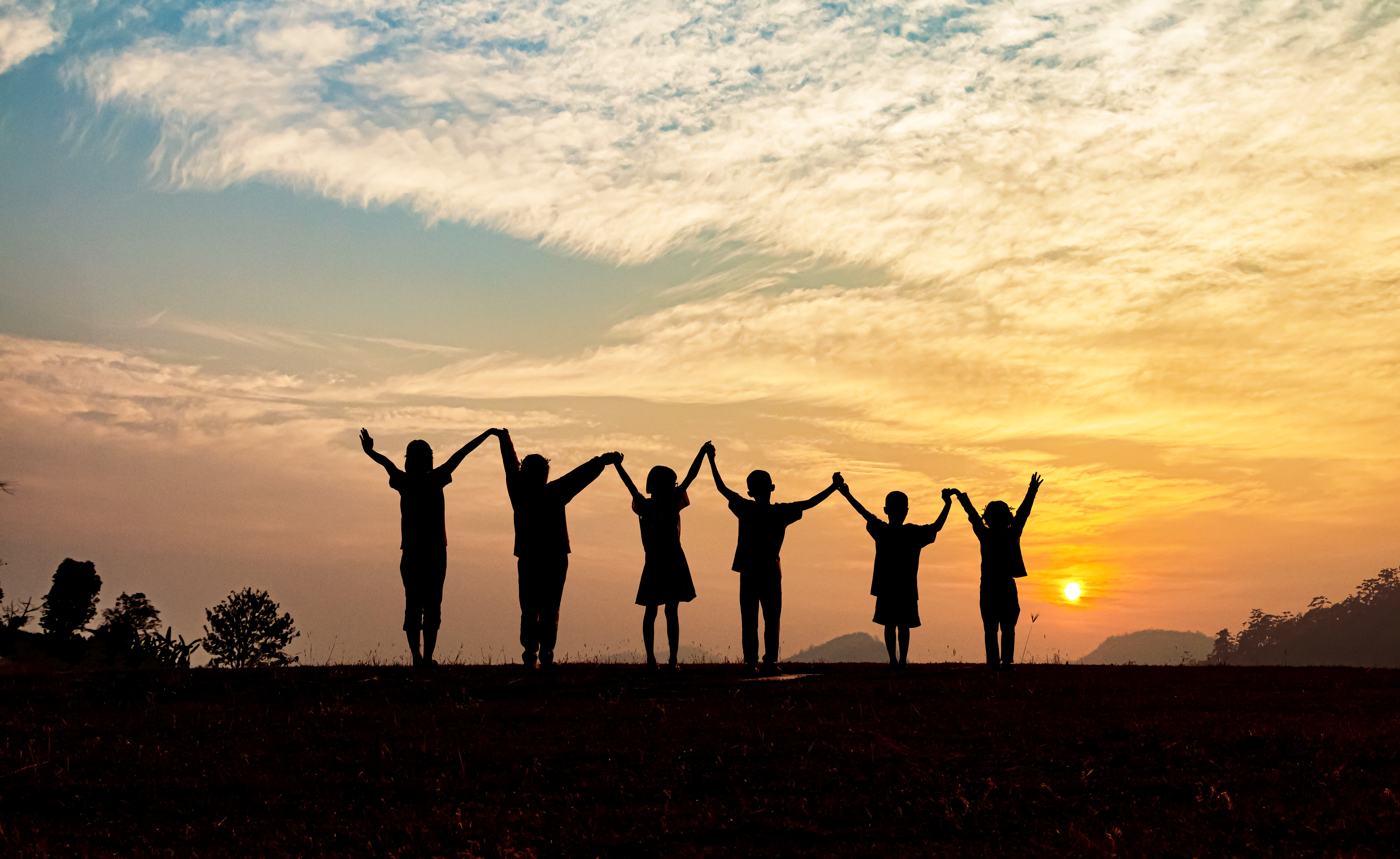 Silhouette of happy children standing with raised hands on the mountain at the sunset time.